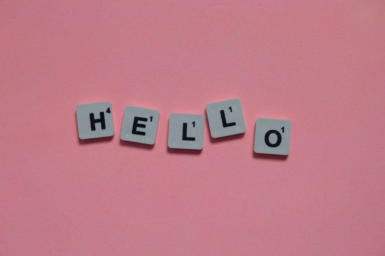 Scrabble tiles arranged to spell 'hello' on a soft pink background, with copy space.