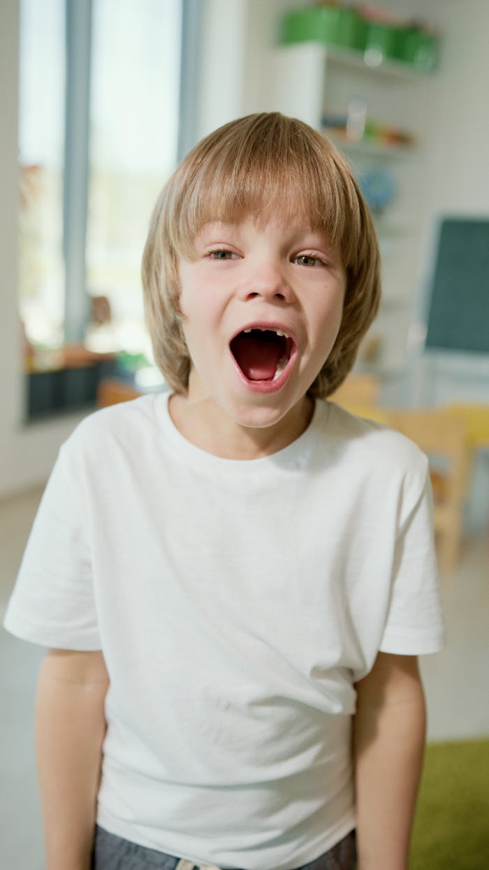 A joyful child with blonde hair laughing in a classroom, wearing a white shirt. Perfect for educational and playful themes.